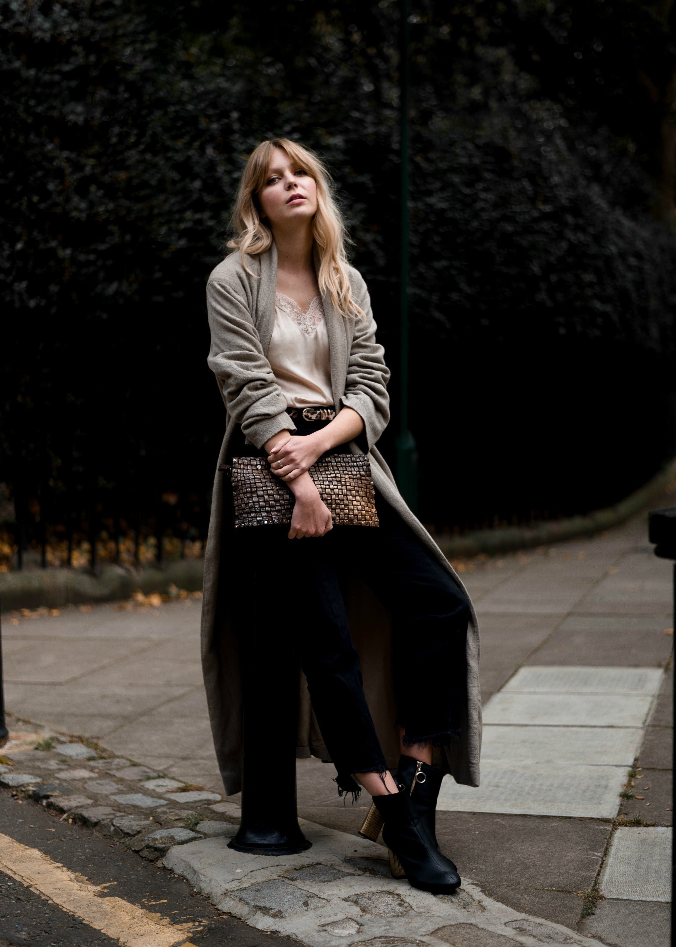 Woman walking outdoors on a street, wearing a long coat and holding a clutch.