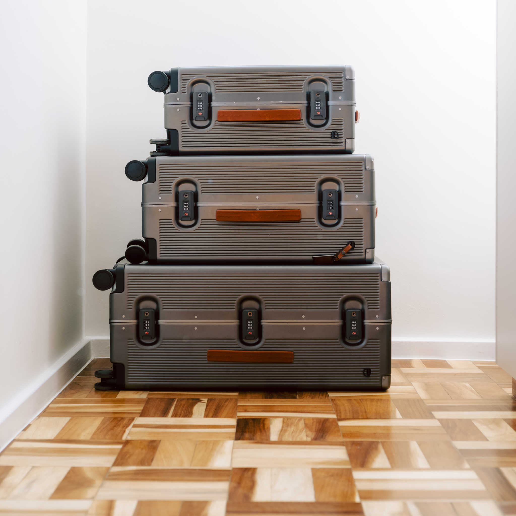 Stack of gray suitcases on a wooden floor against a white wall
