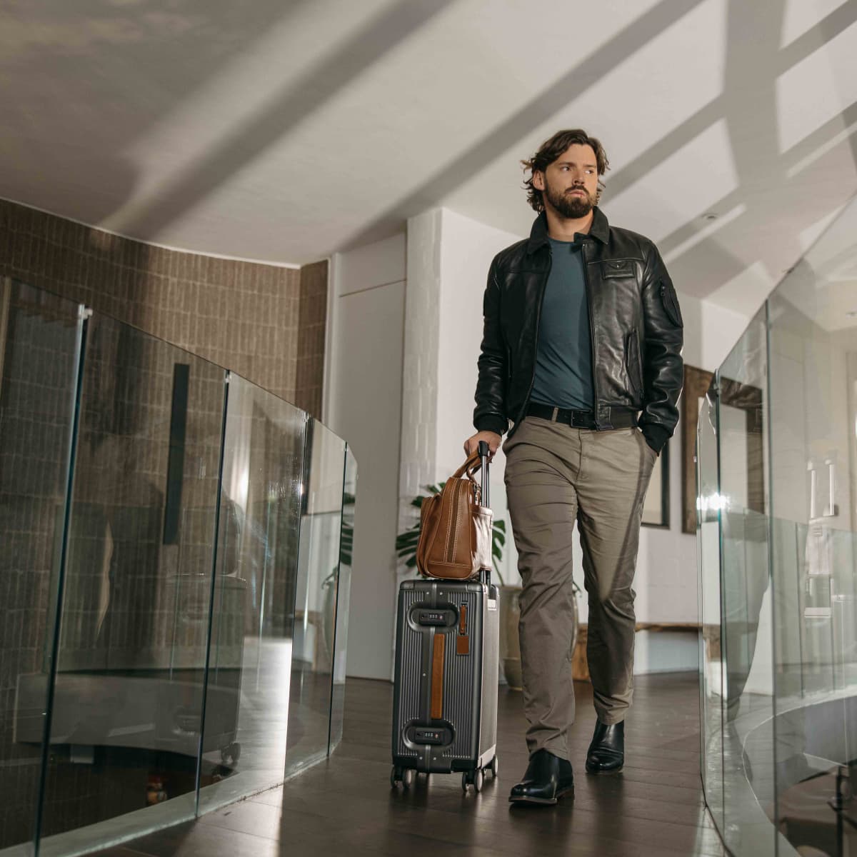 Man wheeling a Jekyll & Hide hard shell Carry-On suitcase with a tan leather bag on the handle