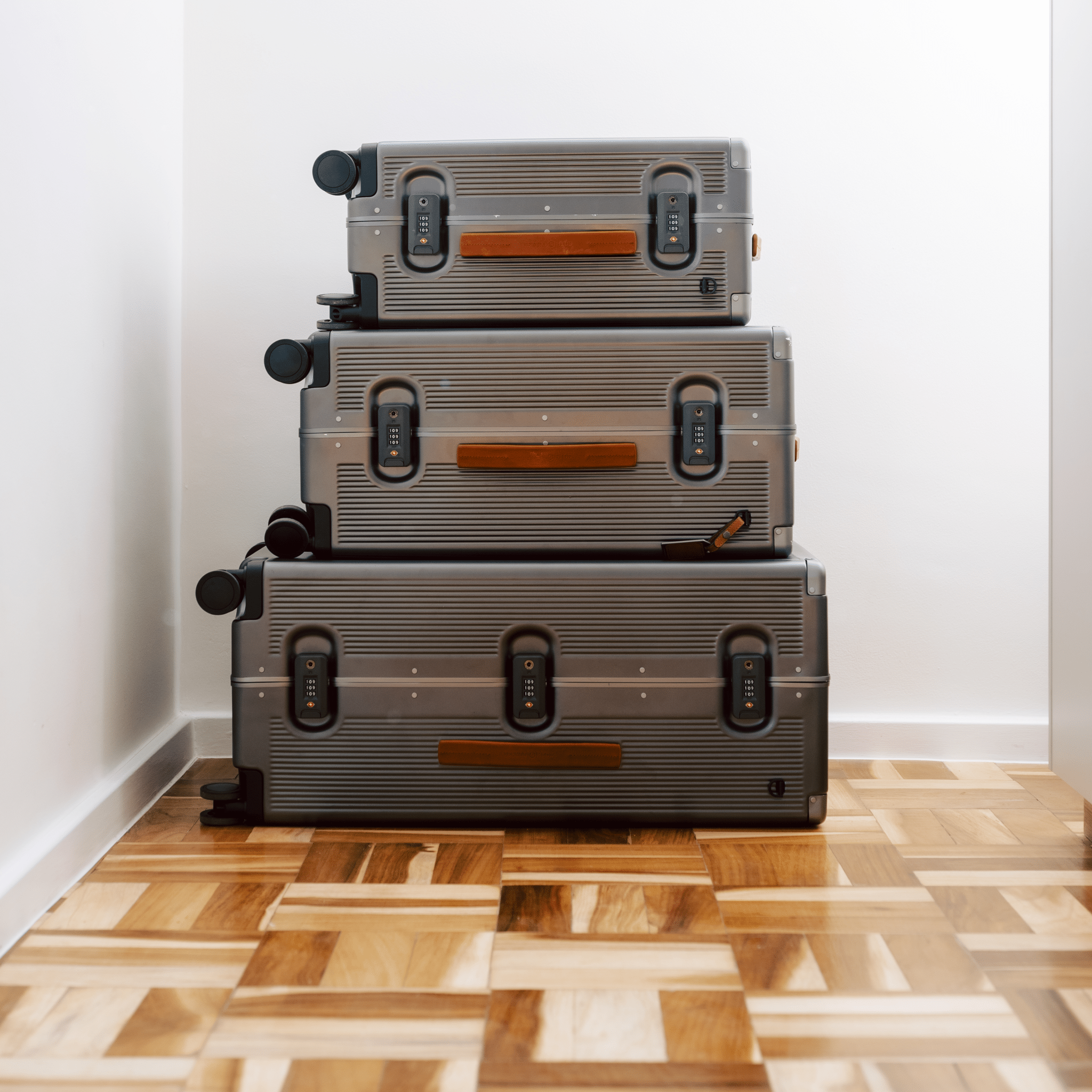Stack of gray suitcases on a wooden floor against a white wall