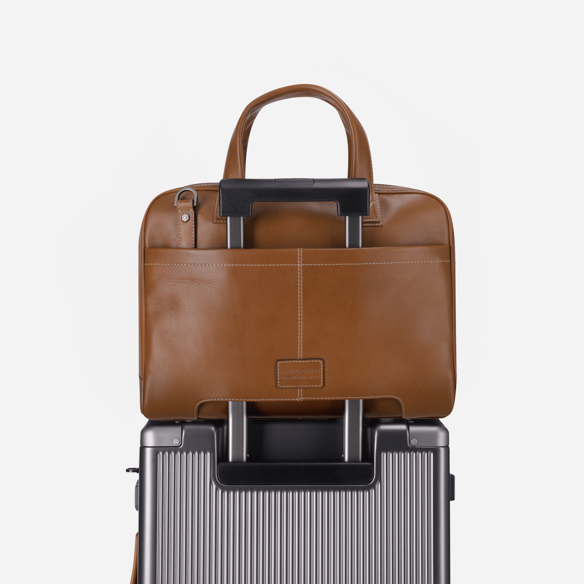 Brown leather briefcase on top of a silver suitcase against a white background
