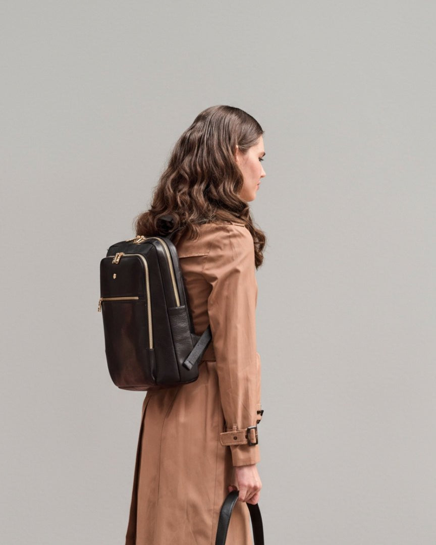 Woman wearing a brown coat with a black backpack on a plain background