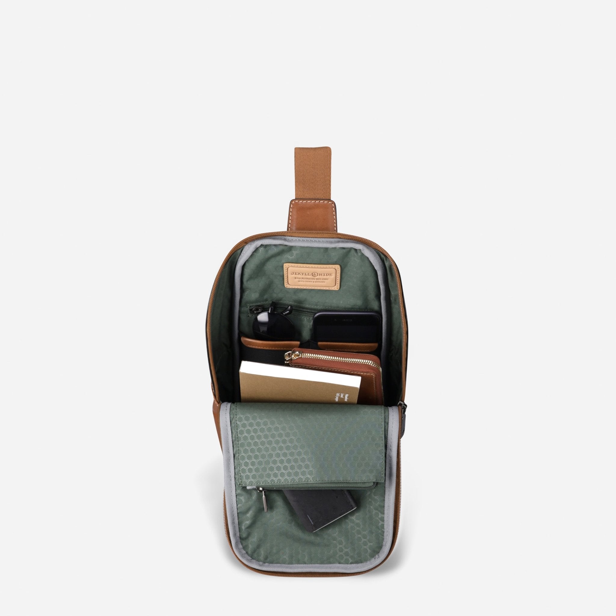 Open Jekyll and Hide tan leather single-strap backpack holding tech, a notebook and wallet